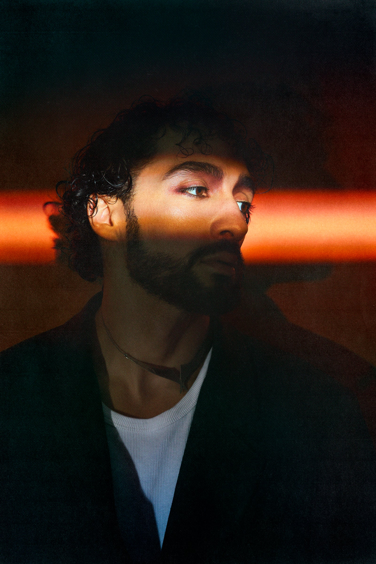 Portrait de Sofiane Pamart éclairé par une bande de néon orange dans le noir