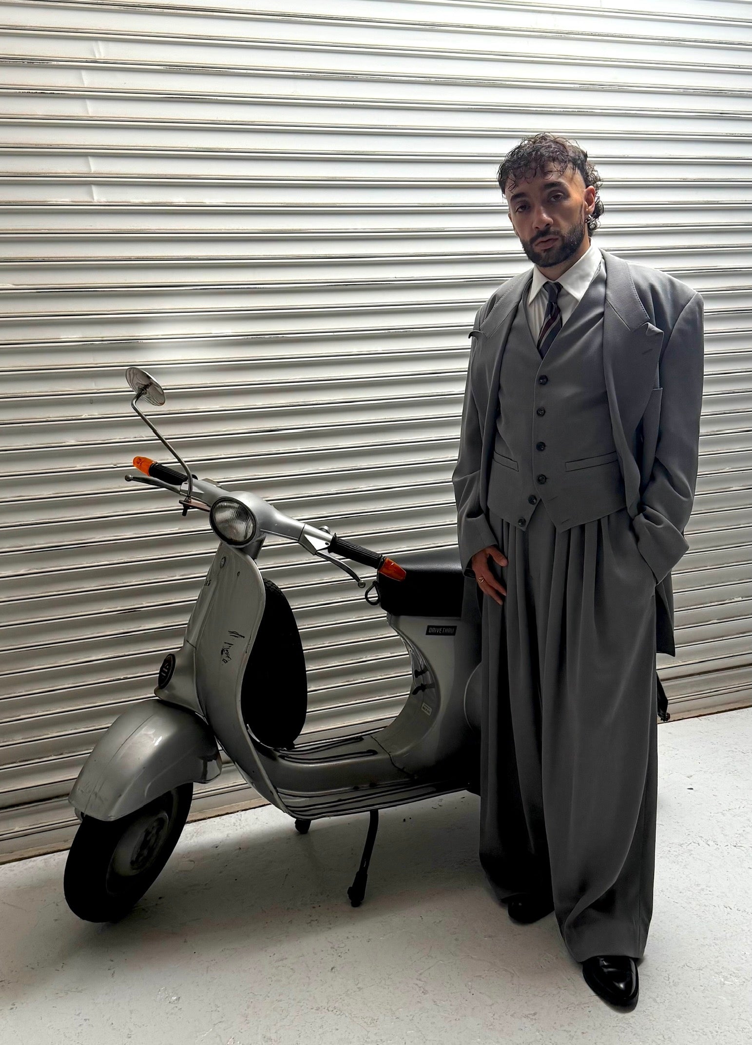 Sofiane Pamart en costume trois-pièces gris à côté d’un Vespa vintage, au Japon