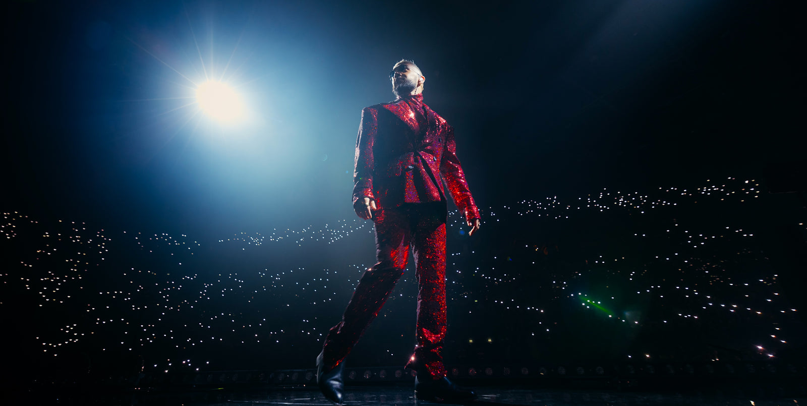 Sofiane Pamart sur la scène d’une arena en costume rouge, la salle constellée de téléphones