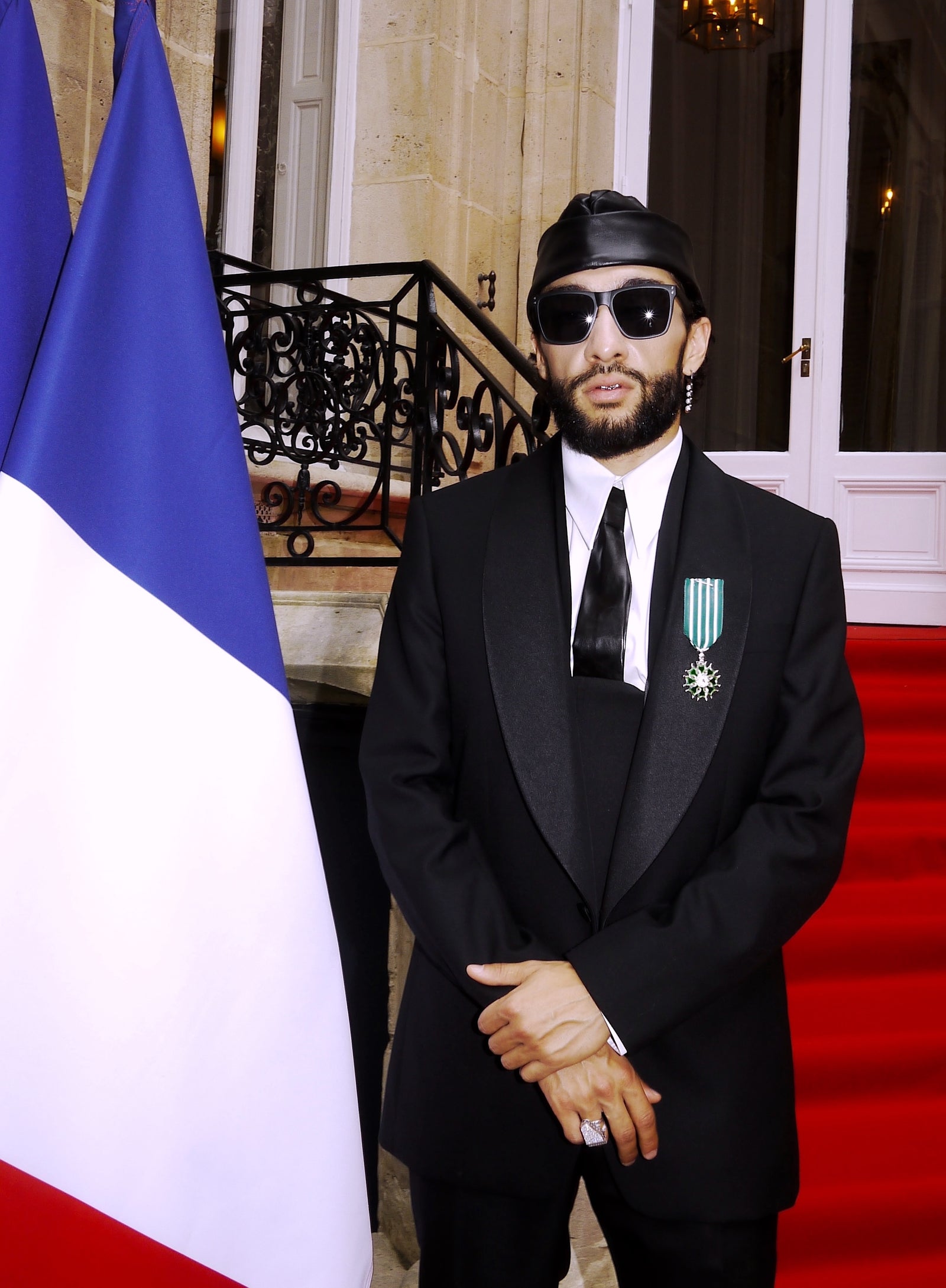 Sofiane Pamart portant sa médaille de chevalier de l’Ordre des Arts et des Lettres, à côté du drapeau français