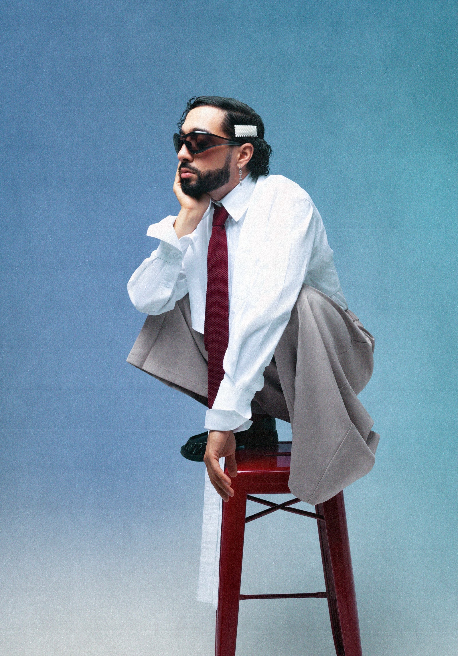 Portrait studio de Sofiane Pamart assis sur un tabouret rouge, en costume gris