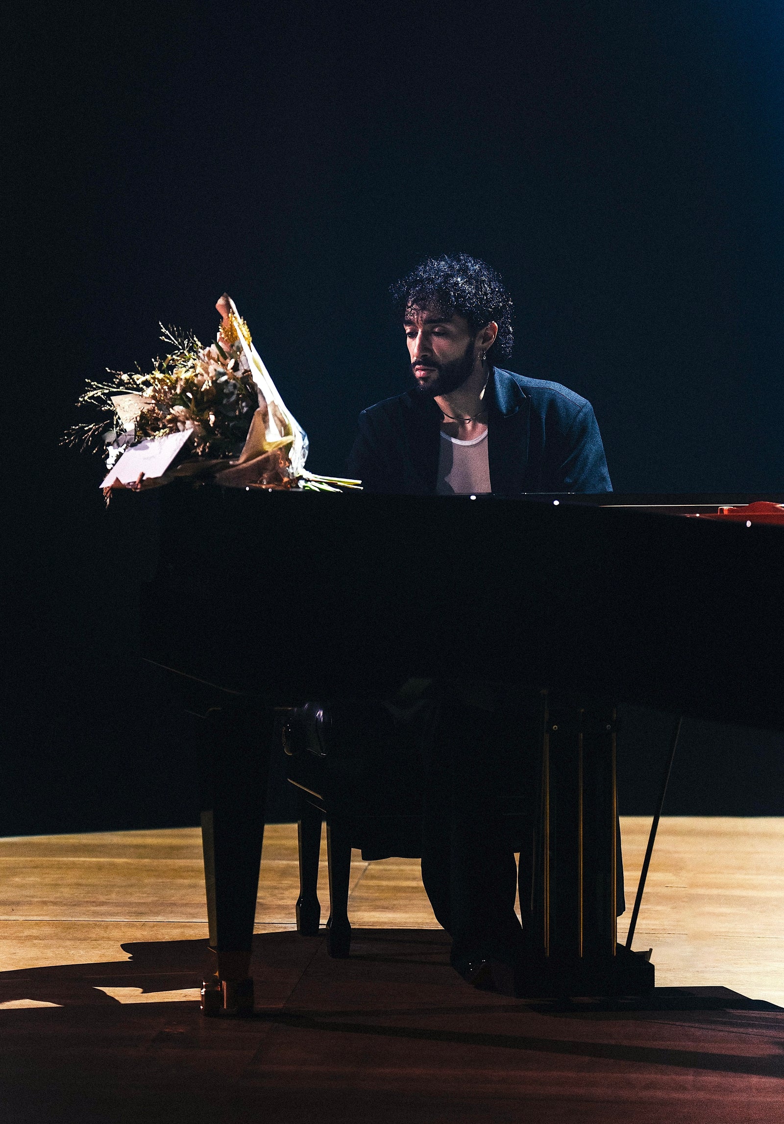 Sofiane Pamart au piano sur une scène dans la pénombre, un bouquet posé sur le couvercle