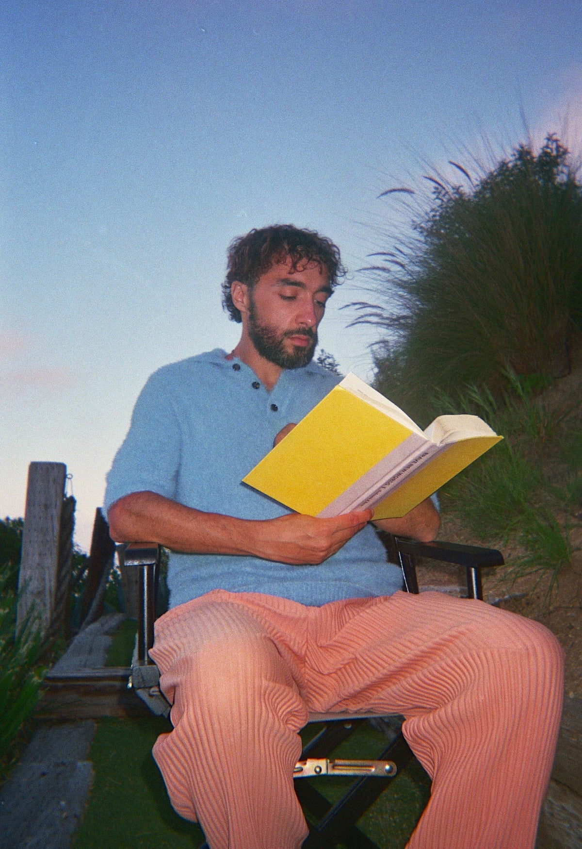 Sofiane Pamart lisant dans un fauteuil de réalisateur au crépuscule, au-dessus des dunes