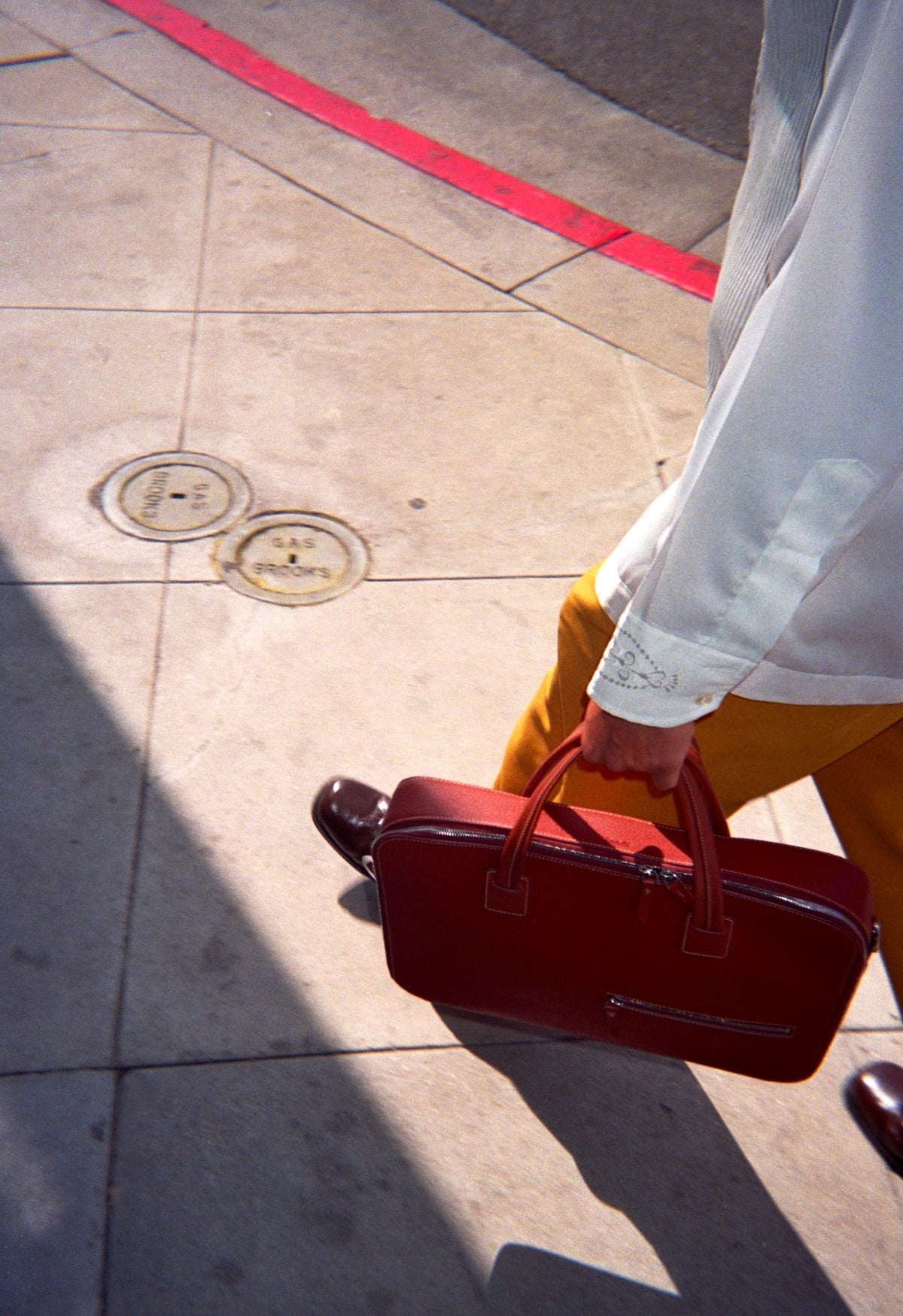 Sofiane Pamart portant un sac en cuir rouge sur un trottoir ensoleillé