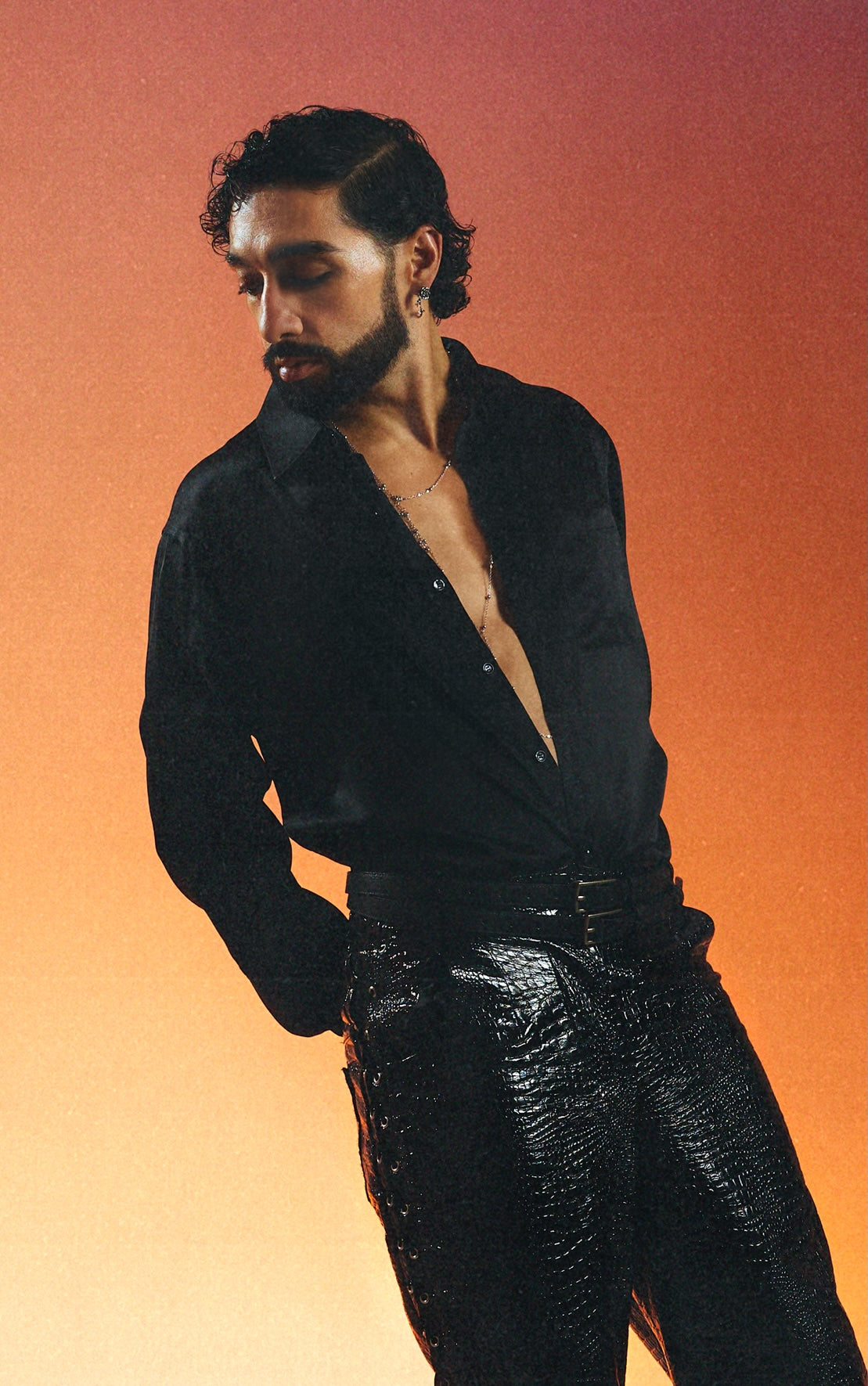 Portrait studio de Sofiane Pamart en chemise noire ouverte sur fond orange